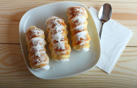 Sweet tubes filled egg white, Czech confection called Kremrole on white plate on wooden table.の写真素材