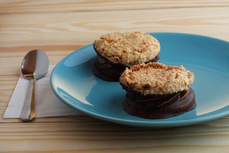 coconut cookies filled jam covered with chocolate on blue plate on wooden table