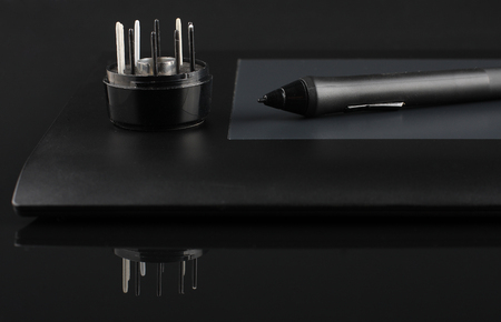 A close-up of  pen on graphic tablet and nibs on stand with reflection on black acrylic sheetの写真素材