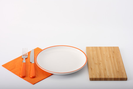 empty white plate and wooden board and fork a knife on white