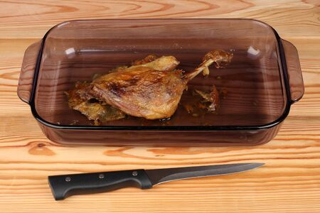 Roast duck in glass pan on wooden table with knifeの写真素材