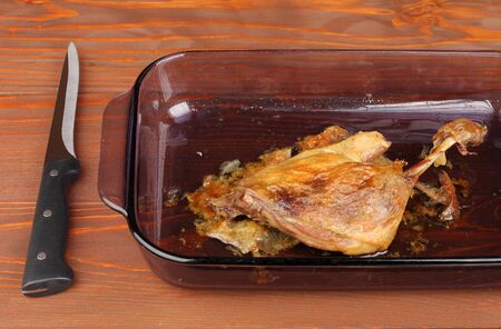 Roast duck in glass pan on wooden table with knifeの写真素材