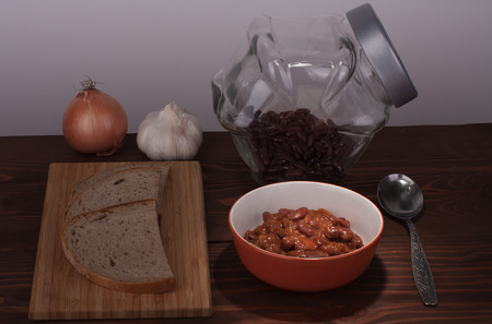 Chili Con Carne in pan on wooden table, on background onion, garlic, bread and beansの写真素材