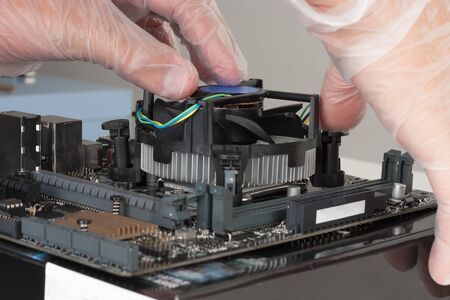 Close up of man hands installing CPU cooler fan on new, modern  motherboard. Thumb pushes the black...