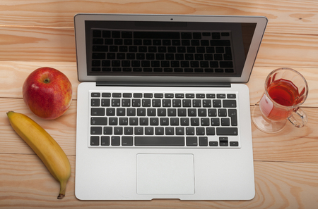 Open modern, new laptop with banana and apple on wooden background, front view, blank black desktop on monitor. の写真素材