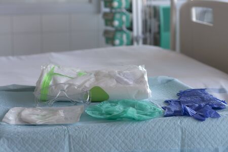 Cap, pair of gloves, plastic protective eyeglasses, respirator ffp2 and coverall clothing  on table in ICU in hospital, personal protective equipment to protect against the virus covid-19.の写真素材