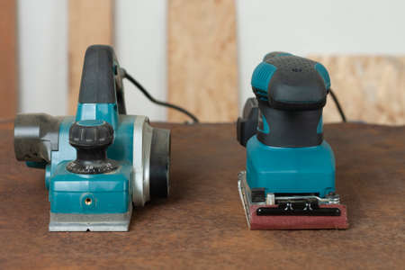 Electric planer and electric sheet finishing sander on old rusty metal sheet, on background oriented...