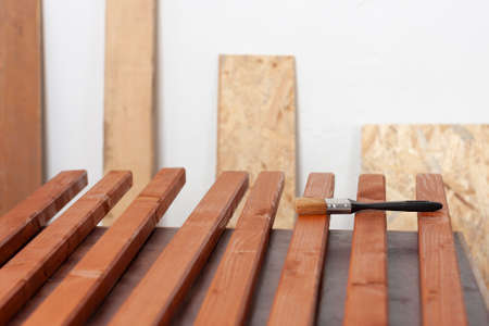 Wooden slats for production of wooden garden bench and paintbrush on table in carpentry workshopの写真素材
