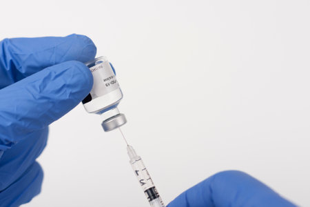 Close up human fingers in gloves, holding covid-19 vaccine vial and syringe with needle. Medical...