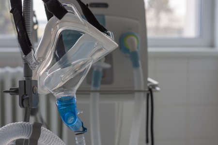 Non-invasive ventilation face mask, side view, on background medical ventilator in ICU in hospital.