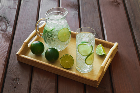 Water drink with lime on wooden tray with ice and condensation on glassの写真素材