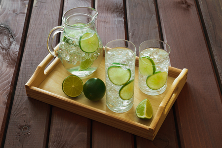 Two water drinks with lime on wooden tray with ice and condensation on glassの写真素材