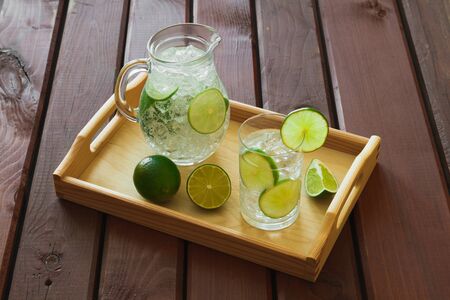 Water drink with lime on wooden tray with ice and condensation on glassの写真素材