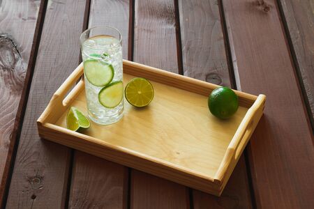 Water drink with lime on wooden tray with ice and condensation on glassの写真素材