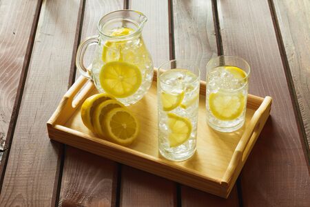 Two water drinks with lemon on wooden tray with ice and condensation on glassの写真素材