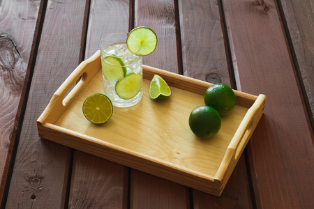 Water drink with lime on wooden tray with ice and condensation on glassの写真素材
