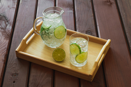 Water drink with lime on wooden tray with ice and condensation on glassの写真素材
