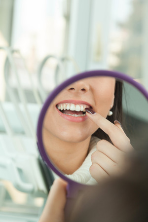 Young woman checking their teeth at mirror after dental treatment - People bodycare and stomatology concept for healthy lifestyle - Focus on girl face - の写真素材