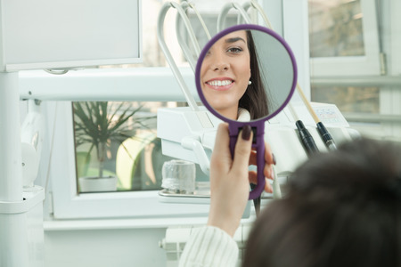 Young woman checking their teeth at mirror after dental treatment - People bodycare and stomatology concept for healthy lifestyle - Focus on girl face - の写真素材