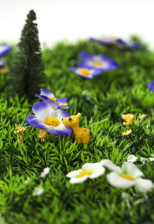 Tiny toy giraffe smelling an artificial flower in a plastic gardenの写真素材