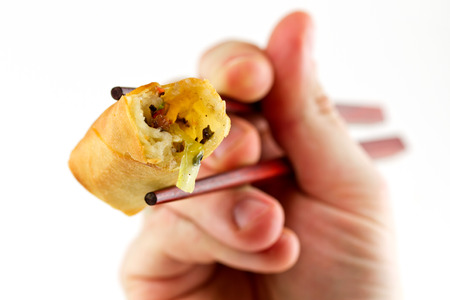 Spring roll on chopsticks held by a handの写真素材