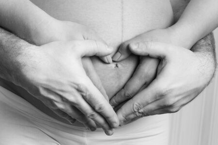 Couple holding hands on pregnant belly in the heart shapeの写真素材