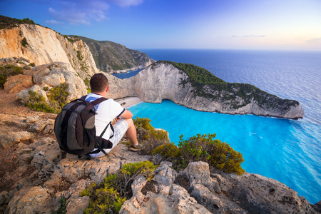 Man with backpack sitting watching sunset over Navagio beach on Zakynthos island, Greeceの写真素材
