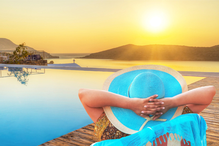 Woman in hat watching sunrise by the poolの写真素材