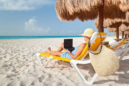 Woman relaxing with laptop under parasol on the beachの写真素材