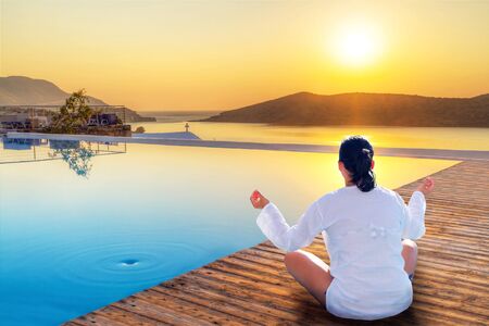 Woman meditating by the pool during sunriseの写真素材