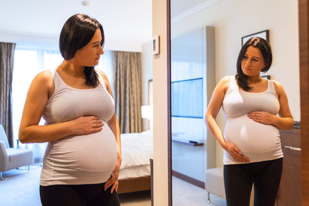 Beautiful pregnant woman looking at the mirrorの写真素材