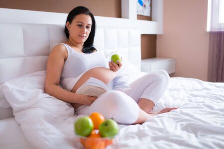 Beautiful pregnant woman reading in bedの写真素材