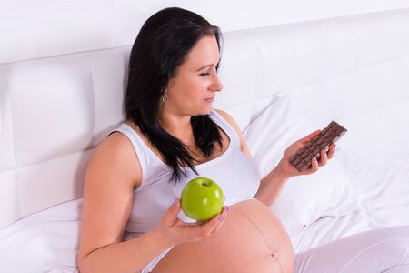 Beautiful pregnant woman with a green apple and chocolate barの写真素材