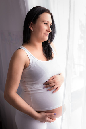 Beautiful pregnant woman portrait at the windowの写真素材
