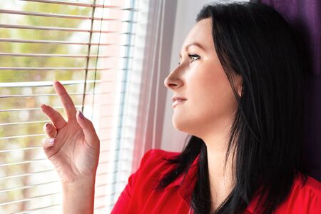 Beautiful woman looking out of the window through a jalousieの写真素材