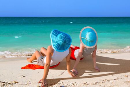 Two women with hats relaxing on the beachの写真素材