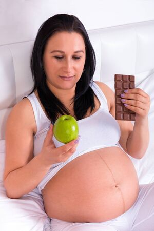 Beautiful pregnant woman with a green apple and chocolate barの写真素材