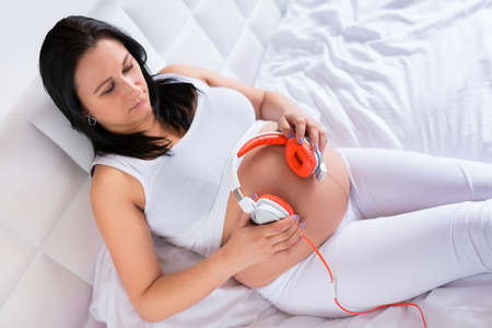 Beautiful pregnant woman playing music for baby with headphonesの写真素材