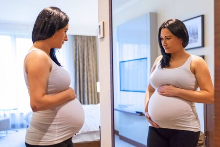 Beautiful pregnant woman looking at the mirrorの写真素材