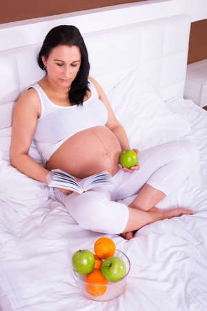 Beautiful pregnant woman reading in bedの写真素材