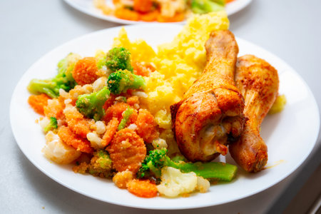 Baked chicken drumsticks with mashed potatoes and vegetables on the plateの写真素材
