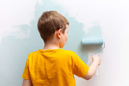 Little boy is painting the walls of his room with a roller in turquoise color.の写真素材