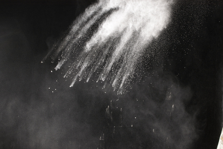 Launched white particle splash on black background. Bizarre forms of of white powder explosion cloud against dark background.の写真素材