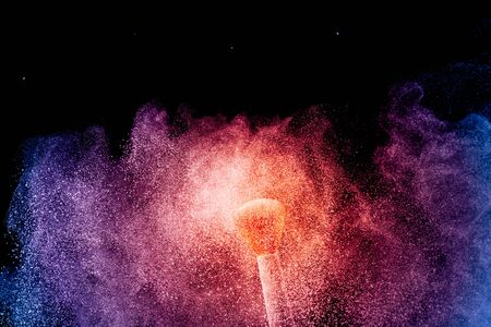 Make-up and beauty concept. Brush with orange blue powder explosion on black background