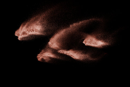 Brown color sand splash against black background. Sand fly wave in the air.