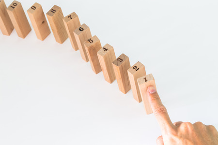 Hand and falling wood pieces dominoes on white backgroundの写真素材