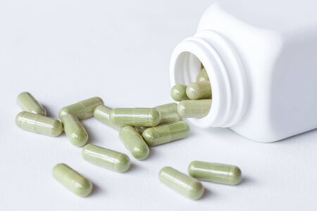 Green Herb capsule out of a white bottle.の写真素材