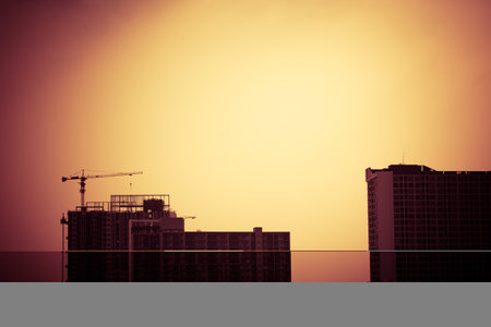 Abstract construction cranes and building silhouettes over sun at sunrise. vintage picture tone.の写真素材