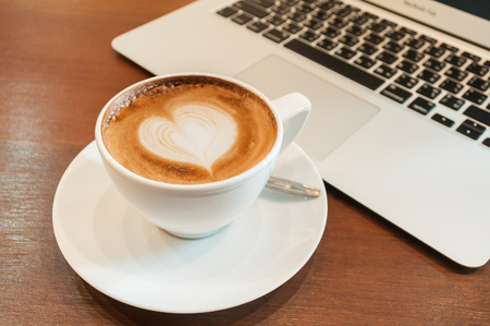 Heart Cappuccino Coffee on the table with computerの写真素材