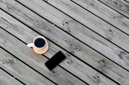 Top view image of Wooden Background with Black Coffee and Black Mobile Phoneの写真素材